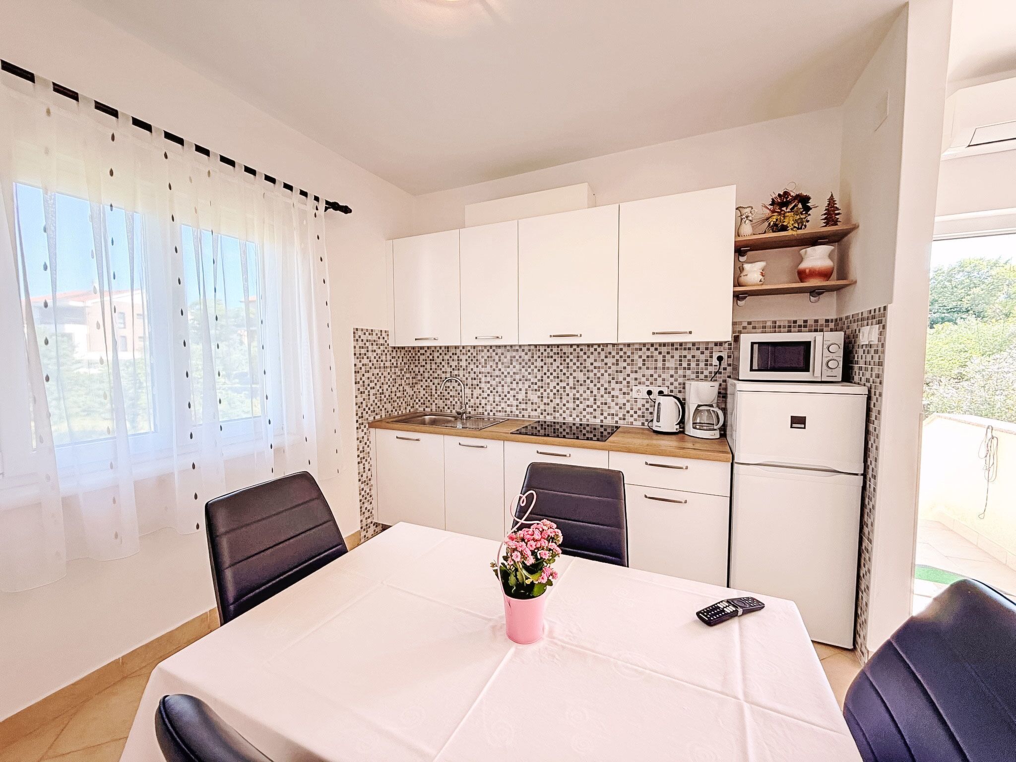 Cozinha compacta com armários brancos, painel de azulejos e área de refeições com mesa posta para dois.