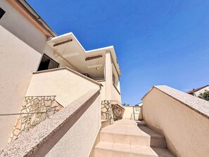 A modern building with a stone facade, a set of stairs leading to a second floor, and a clear blue sky. - Apartment Nevenka by Interhome (Polje)