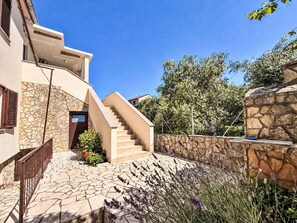 A modern building with a stone facade, a staircase leading to the entrance, and a stone wall with plants. - Apartment Nevenka by Interhome (Polje)