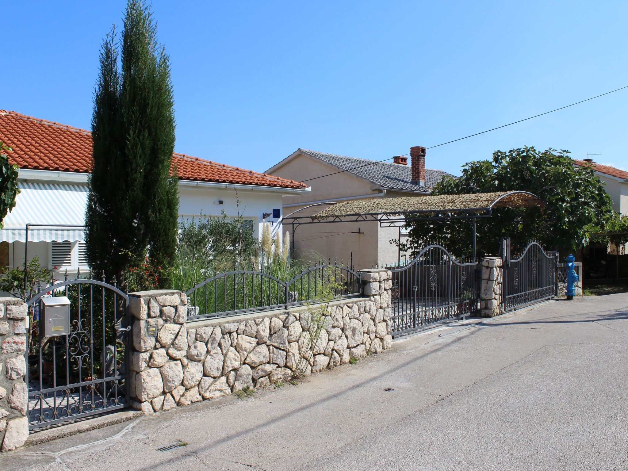 A residential street with stone walls, metal gates, and houses with red-tiled roofs.