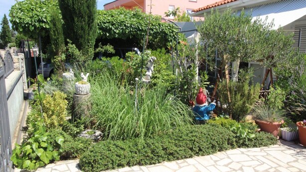 A garden with various plants and a statue of a figure. - Apartment Renata by Interhome (Polje)