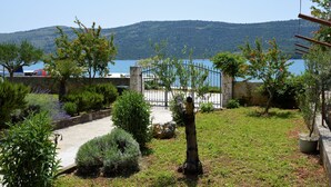 Ein Garten mit Steinmauer, einem Weg und Blick auf See und Berge.