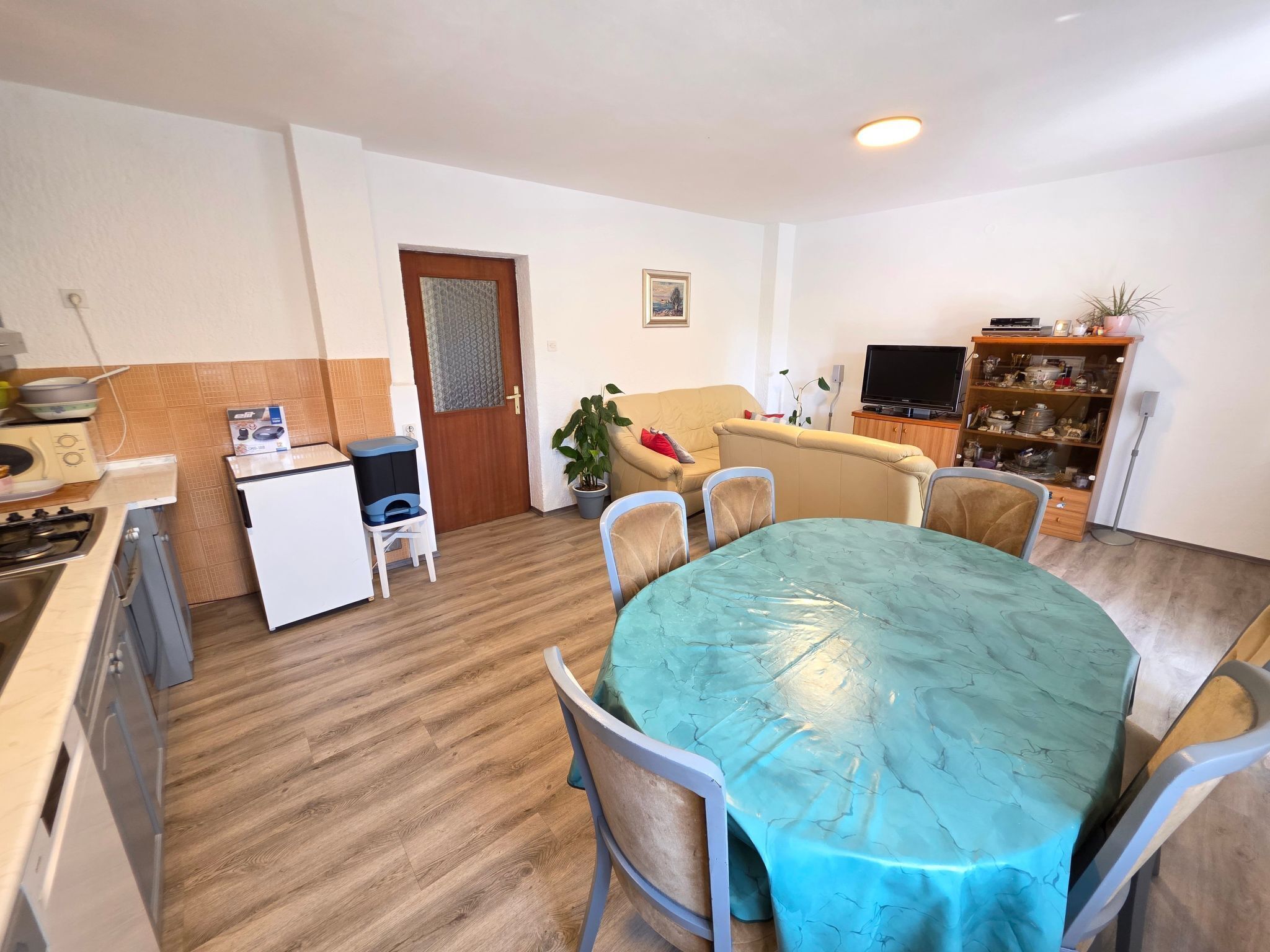 A compact living space with a dining table, chairs, a sofa, a TV, and a kitchen area with a stove and refrigerator.