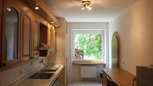 Una cocina compacta con armarios de madera, horno empotrado, lavamanos y ventana con vistas a la vegetación.