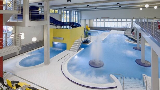 Una piscina interior con tobogán, varios niveles y una fuente de agua.