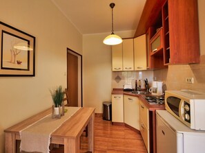 A compact kitchen with wooden cabinets, a dining table with a bench, and a hanging light fixture. - "Helena2" mit Blick auf das Wasser by Interhome (Dubrovnik/Mlini)