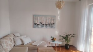 Ett vardagsrum med en soffa, ett soffbord, ett litet sidobord, en krukväxt och en tavla som föreställer segelbåtar.