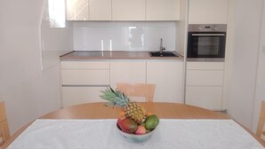 Ett modernt kök med vita skåp, en diskho i rostfritt stål och en ugn. En fruktskål med ananas, mango och avokado står på matbordet.