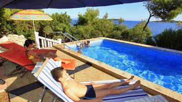 A poolside area with lounge chairs, a pool, and a view of the sea.