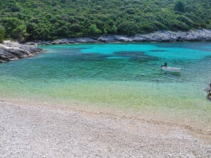 A clear turquoise sea with a boat on the right, rocky shore, and dense green forest in the background. - Villa Nova by Interhome (Blato)