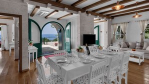 A dining area with a white table set for six, wooden beams on the ceiling, and a view of the sea through an archway. - Villa Miscic by Interhome (Brela)