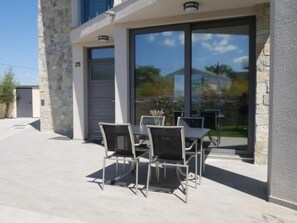 Ein modernes Gebäude mit Steinverkleidung, einem Glastür-Eingang und einer Terrasse mit Gartenmöbeln.
