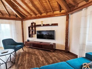 A living room with a wooden ceiling, a flat-screen TV mounted on a wall, a blue sofa, a blue armchair, and a small round table. - Das Haus der Weinkellerei by Interhome (Cabo da Praia)