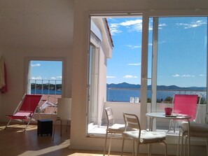 Ein Balkon mit Blick auf Meer und Berge, ausgestattet mit Stühlen und einem Tisch.