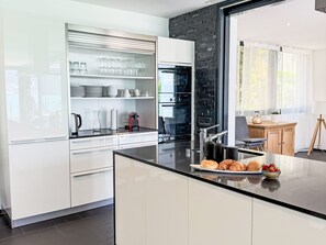 Eine moderne Küche mit weißen Schränken, einer schwarzen Arbeitsplatte und Blick ins Freie.