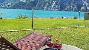 En terrasse med udsigt til en sø og bjerge, et træbord og to glas rød drik.