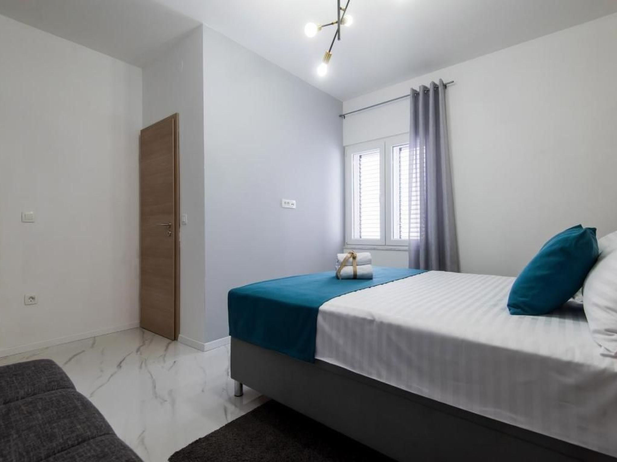 A bedroom with a bed, a window with curtains, a bedside table, and a door.