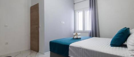 A bedroom with a bed, a window with curtains, a bedside table, and a door.