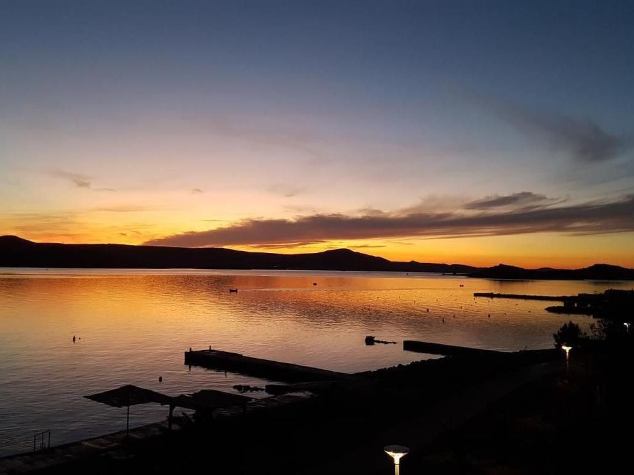 Un lac paisible au coucher du soleil, avec une jetée et des parasols.