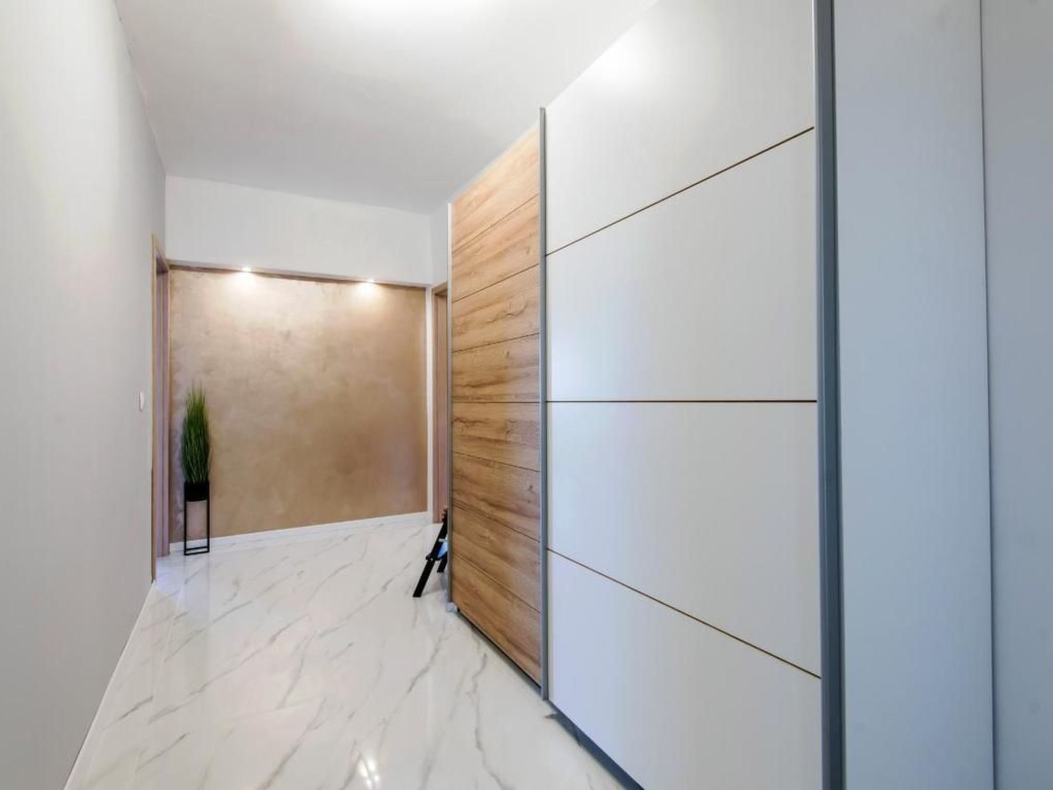 A hallway with a marble floor, a wooden panel wall, and a potted plant.