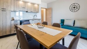 A modern kitchen with wooden cabinets, a dining table with chairs, and a blue sofa in the living area. - Wohnung in Turanj mit Grill by Interhome (Donje Rastane)