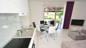 Una cocina moderna con estufa integrada, un comedor con mesa y sillas, y una sala de estar con sofá y televisor.