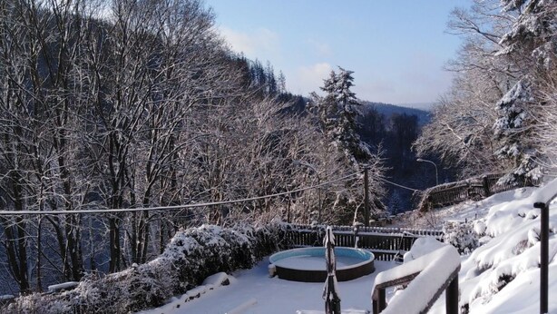 Un espacio exterior cubierto de nieve con piscina, terraza de madera y vista a una ladera boscosa.