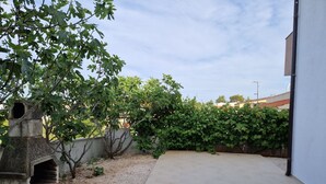 Eine gepflasterte Terrasse mit einem Grill aus Stein und einer Hecke.