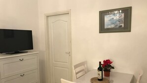 A room with a television on a dresser, a dining table with a chair, a framed picture on the wall, and a bottle of wine on the table. - Ferienwohnung by Interhome (Orebić)