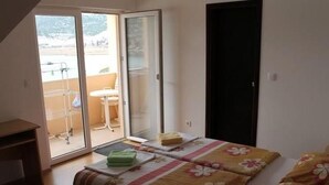 Une chambre à coucher comprenant un lit, un bureau et une porte-fenêtre coulissante donnant sur un balcon.