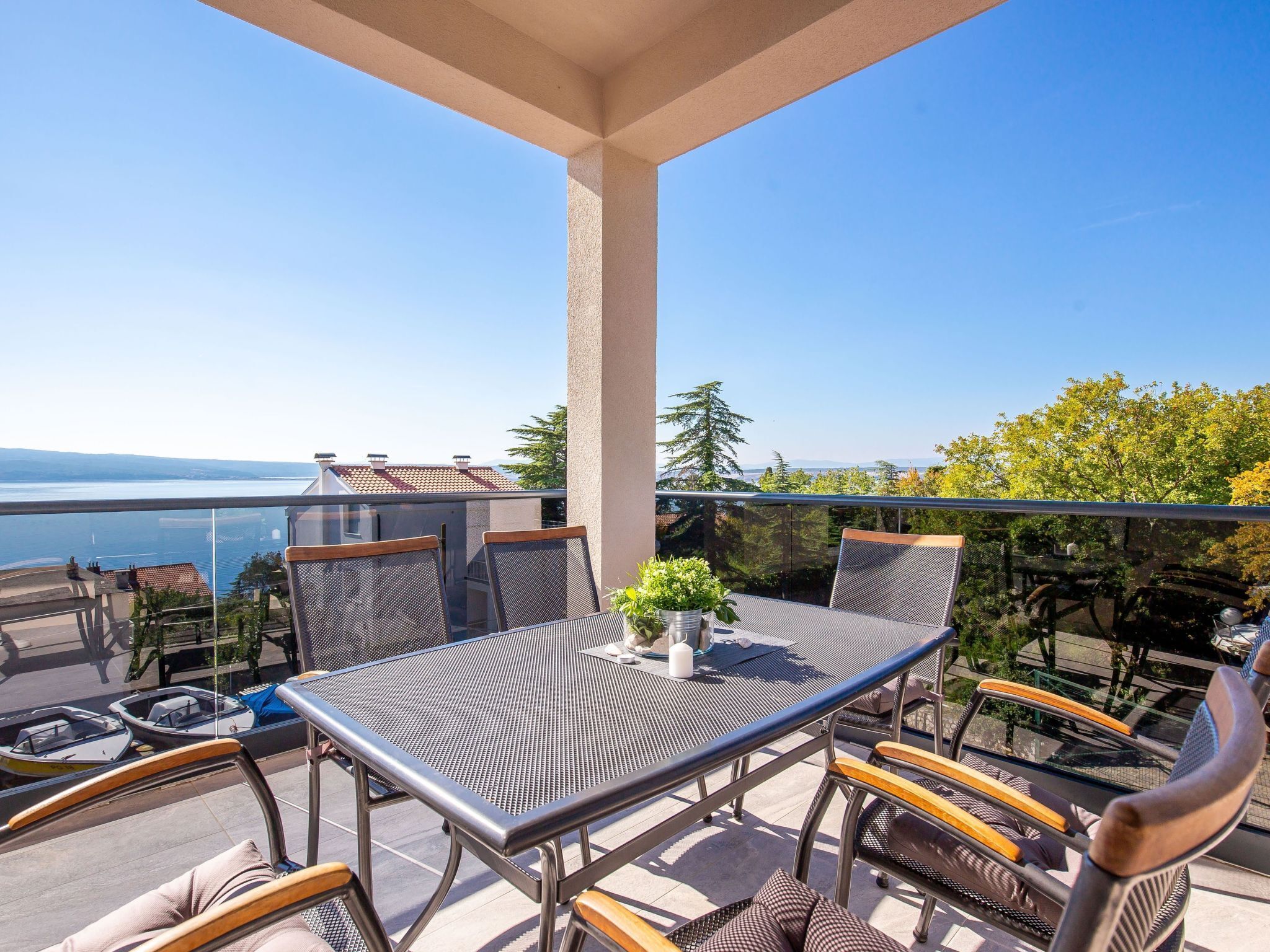 Ein Balkon mit Tisch und Stühlen, mit Blick auf ein Gewässer und Bäume.