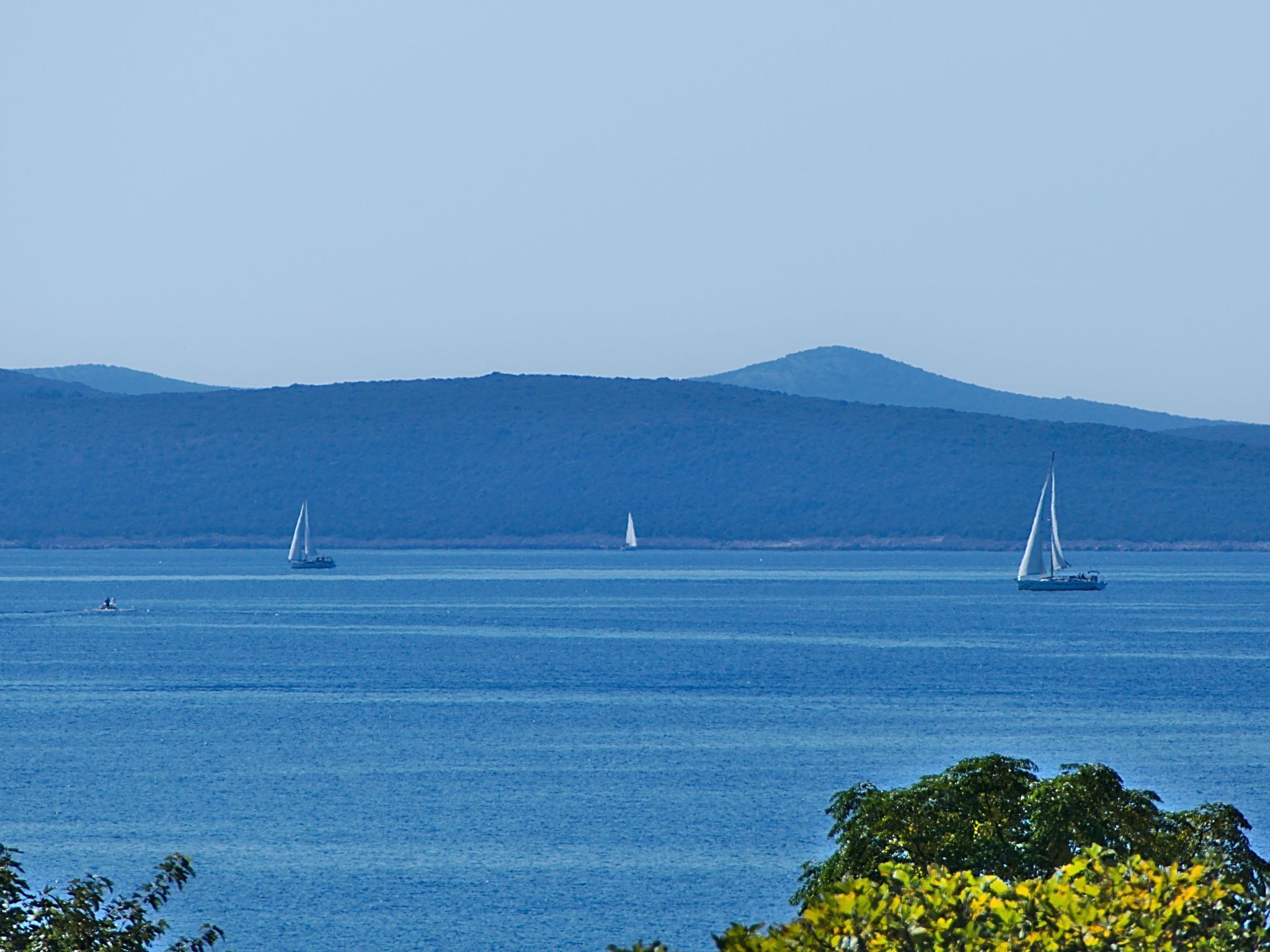 Blick auf die Küste mit Segelbooten auf dem Wasser und einem Berg im Hintergrund.
