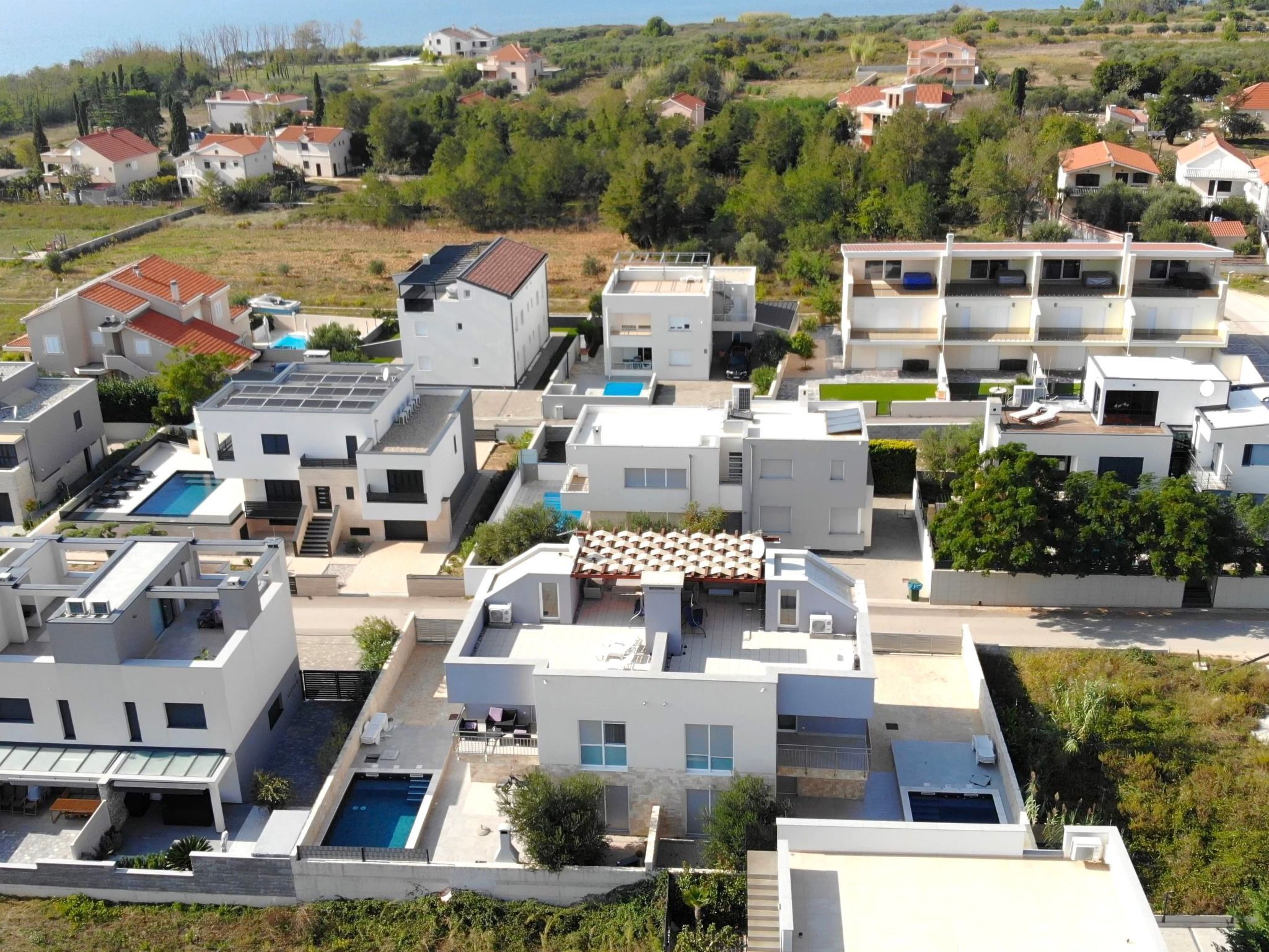 A residential area with modern houses, a swimming pool, and a view of the sea.