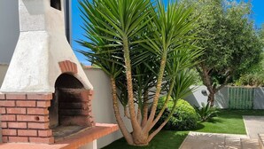 Eine Terrasse mit einem gemauerten Außenofen, grünem Kunstrasen und einer Palme.