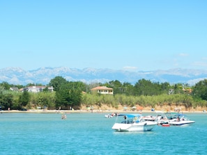 A coastal scene with boats on the water, a beach with people, and mountains in the background. - Erdgeschoss-Ferienwohnung mit Garten und Pool by Interhome (Privlaka)