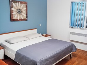 Ein Schlafzimmer mit einem Bett, einem Nachttisch, einer Wanduhr, einem Fenster mit Jalousien und einer Heizung.