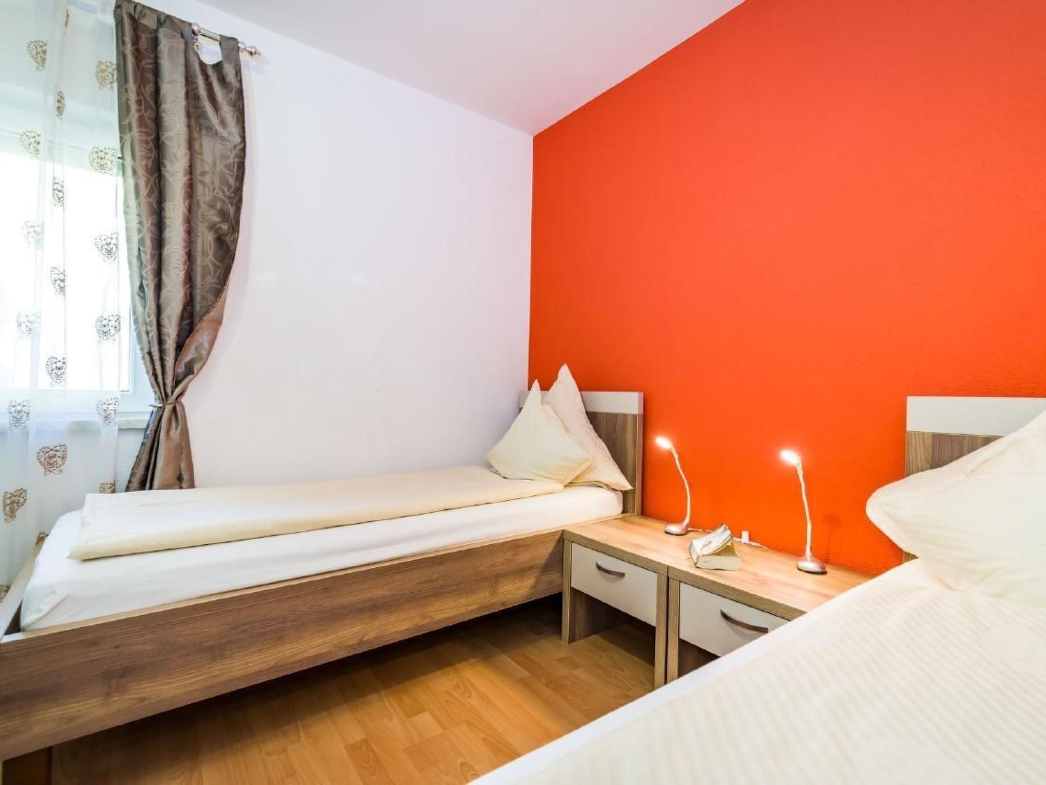 A bedroom with a bed, bedside table, lamp, and a window with curtains.