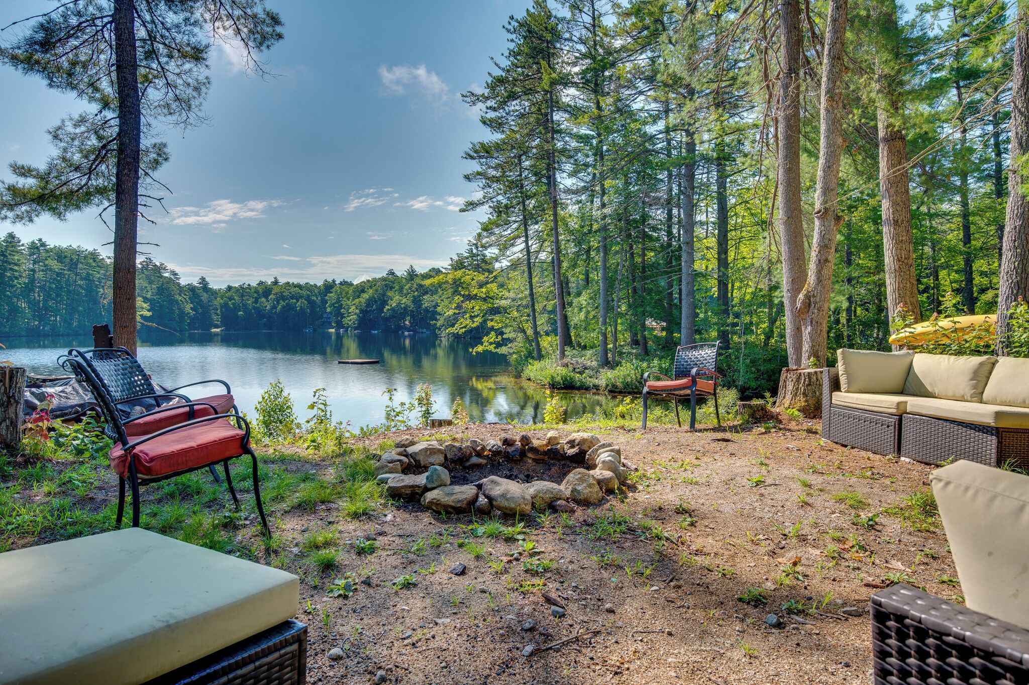 A lakeside outdoor seating area with a fire pit, chairs, and a sofa.