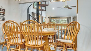 A dining area with a wooden table and chairs, a spiral staircase, and a view of the outdoors through large windows. - Waterfront Wakefield Retreat w/ Floating Dock (Sanbornville)