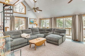 A spacious living room with a large sectional sofa, a wooden coffee table, a spiral staircase, and large windows with curtains. - Snowmobile Trails & Ice Fishing in Wakefield (Sanbornville)