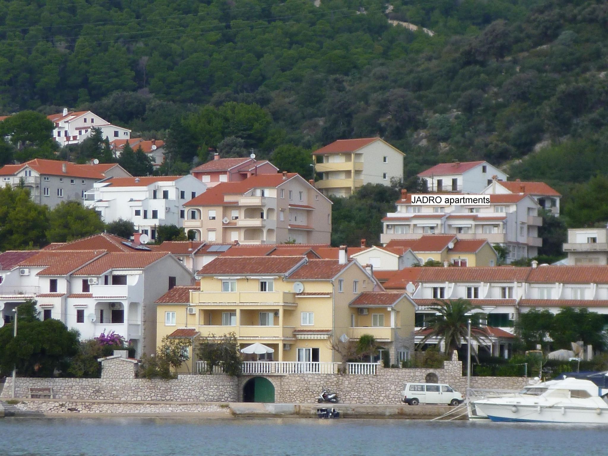 A coastal residential area with multi-story buildings, a stone wall, and a small green archway.