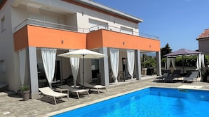 Une piscine entourée de chaises longues et de parasols, le tout bordé par un bâtiment aux murs orange et blancs.