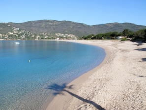 A beach with clear blue water, sandy shore, and a backdrop of hills with buildings. - Casa Enorati - Direkter Zugang zum Meer by Interhome (Sagone)