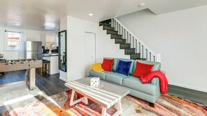 Ein modernes Wohnzimmer mit einem Kicker, einer Couch mit bunten Kissen, einem Couchtisch und einer Treppe.