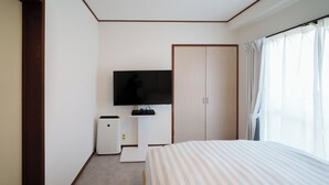 Quarto de hotel com cama, televisão, guarda-roupa e pequena escrivaninha com aquecedor.