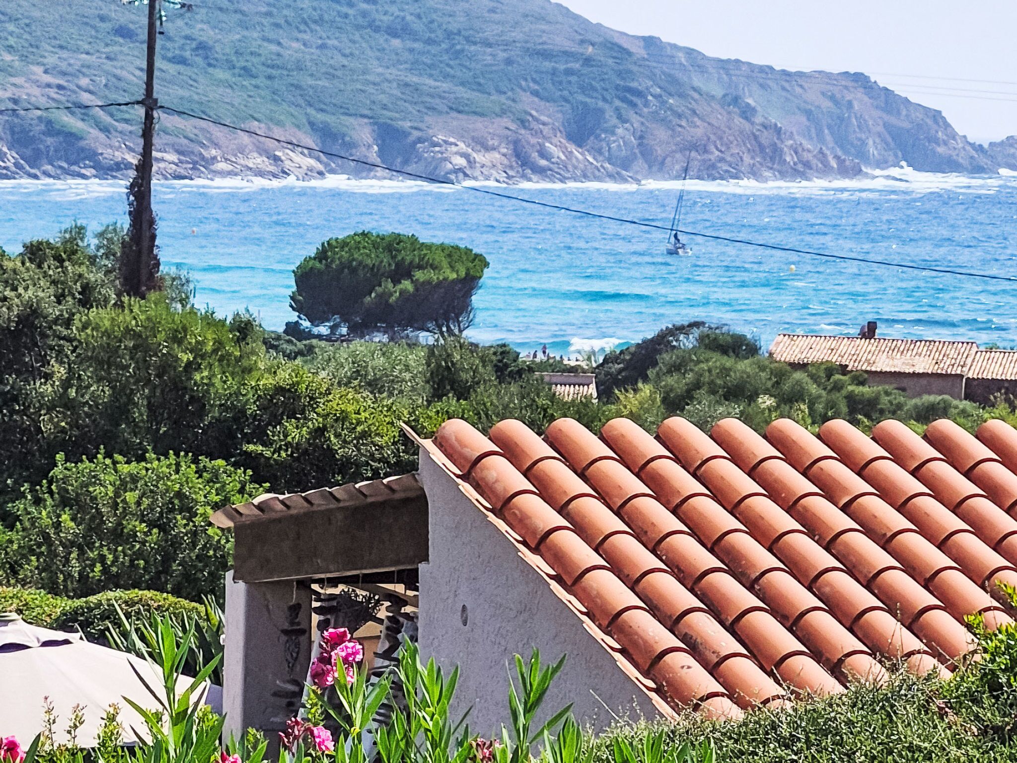A coastal landscape with a rocky cliff, a small building with a tiled roof, and a view of the sea.