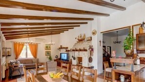 Un comedor con mobiliario de madera, una mesa con fruta y una zona de cocina con una planta y una estufa.