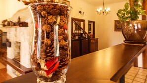 Un florero de vidrio lleno de piñas y adornos sobre una mesa de madera en una habitación con chimenea, escalera y candelabro.