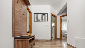 Un couloir avec un plancher en bois, un banc sur lequel est posé un chapeau, et un miroir accroché au mur.