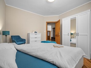 A bedroom with a bed, a blue chair, a white dresser, and a wardrobe. - Vivento by Interhome (Plomin)